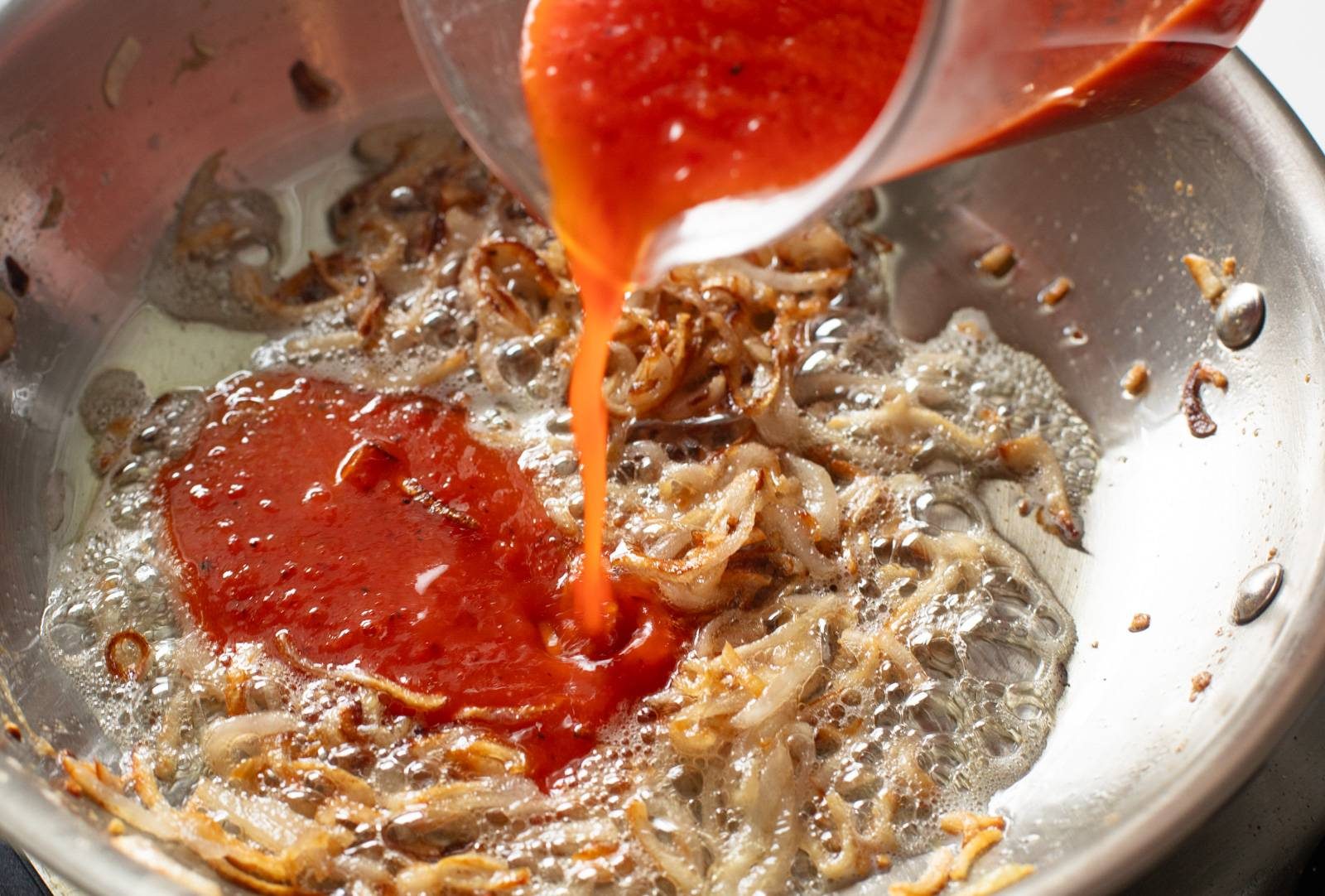 Adding red pepper puree to pan.