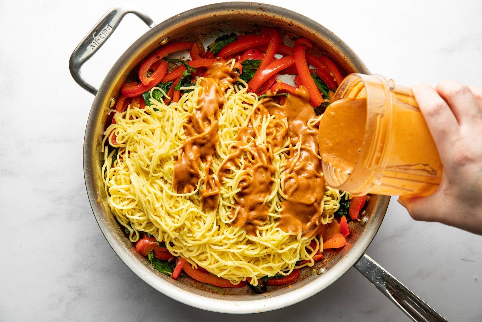 Adding peanut sauce to noodles and veggies in a pan.