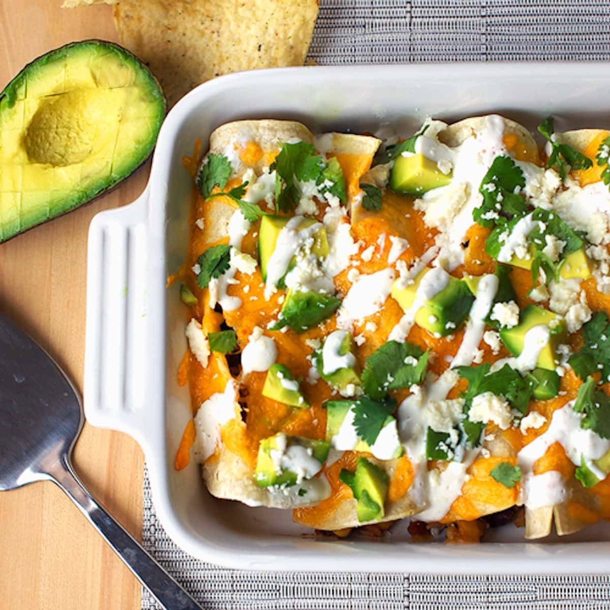 Chicken enchiladas in a white baking dish with half an avocado.