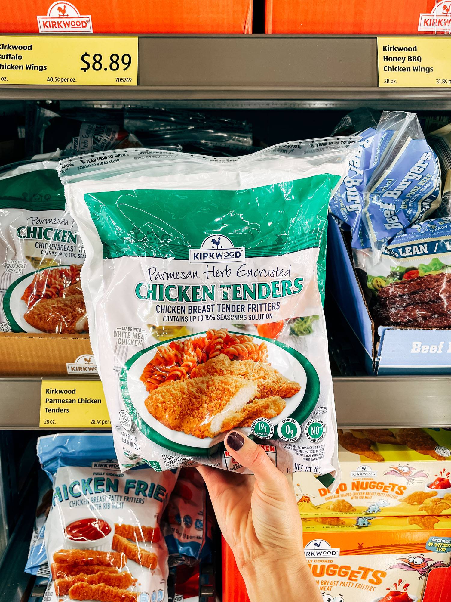 White hand holding a bag of frozen chicken tenders