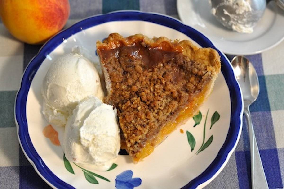 Peach pie on a plate with vanilla ice cream.